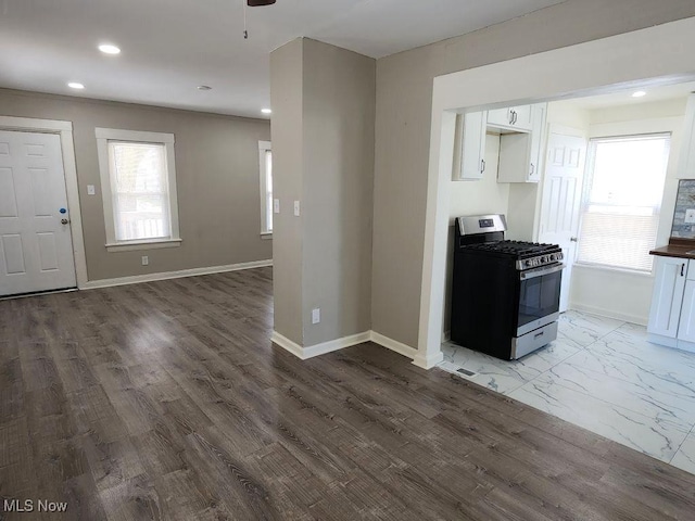 kitchen featuring recessed lighting, stainless steel gas range oven, white cabinetry, and baseboards