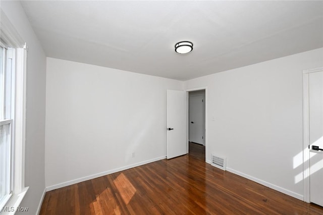 empty room with baseboards, visible vents, and wood finished floors