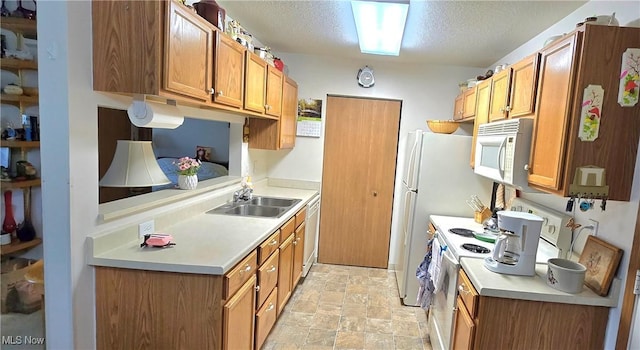 kitchen featuring a textured ceiling, light countertops, stone finish flooring, white appliances, and a sink