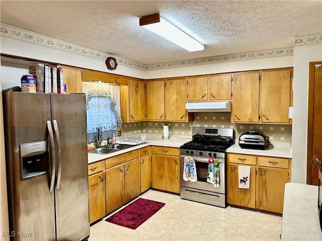 kitchen featuring a sink, under cabinet range hood, light countertops, a textured ceiling, and appliances with stainless steel finishes