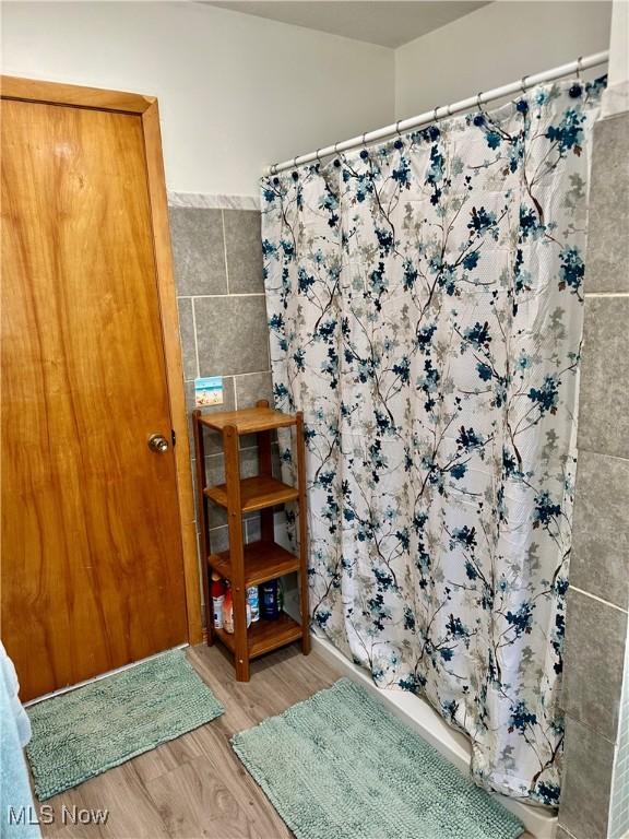 full bath with tile walls, wood finished floors, and a shower with shower curtain