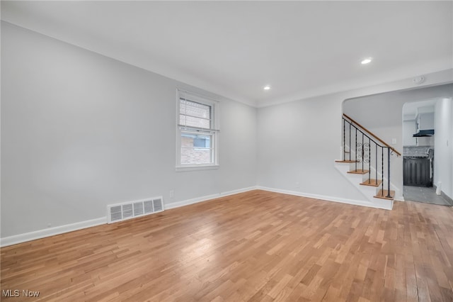 empty room with light wood-style flooring, baseboards, stairway, and visible vents