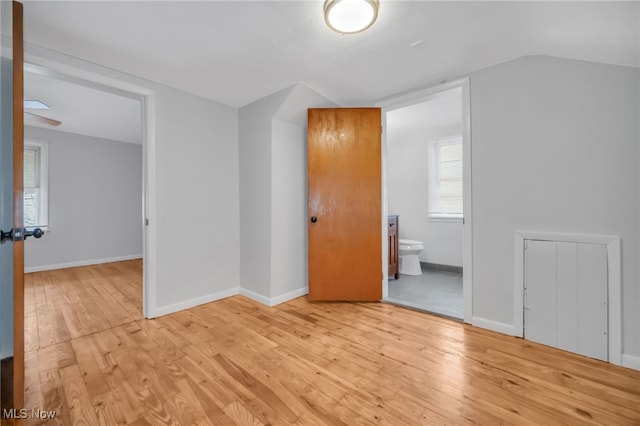 unfurnished bedroom featuring ensuite bath, baseboards, lofted ceiling, and light wood-type flooring
