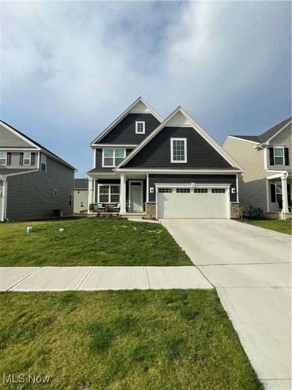craftsman-style home with a porch, driveway, a front yard, and stone siding