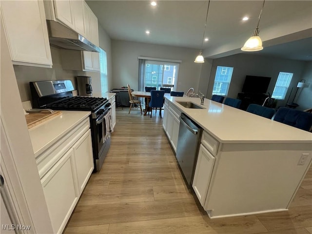 kitchen with white cabinets, under cabinet range hood, appliances with stainless steel finishes, light wood finished floors, and a sink