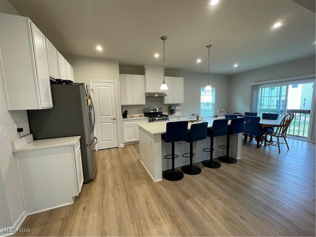 kitchen with light wood-type flooring, under cabinet range hood, a kitchen bar, appliances with stainless steel finishes, and a sink