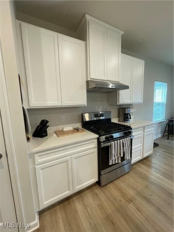 kitchen featuring light wood-type flooring, white cabinets, under cabinet range hood, light countertops, and stainless steel gas range oven
