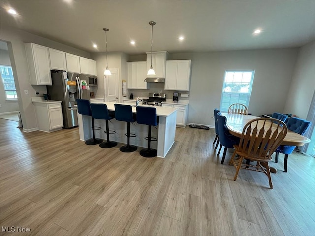 kitchen with white cabinets, appliances with stainless steel finishes, under cabinet range hood, light countertops, and light wood finished floors