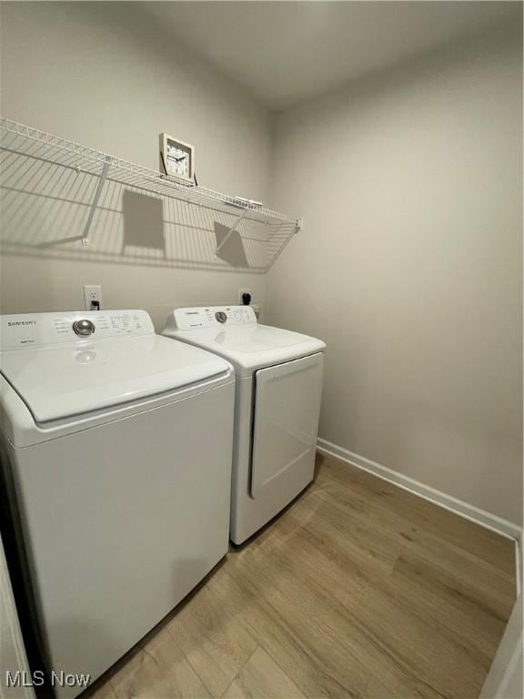 clothes washing area featuring washing machine and dryer, laundry area, baseboards, and light wood-style flooring