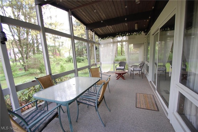 sunroom featuring outdoor dining area and beamed ceiling