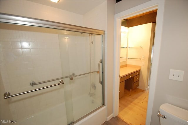 bathroom with combined bath / shower with glass door, toilet, and wood finished floors