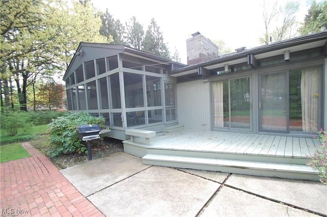 rear view of property featuring a sunroom, a chimney, and a deck