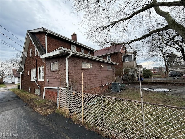 view of side of home featuring a chimney, fence, and central AC