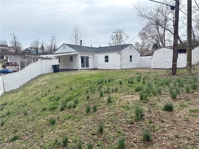 back of property with an outbuilding, a fenced backyard, a storage shed, an attached carport, and a lawn