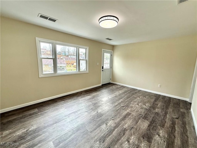 empty room featuring dark wood-type flooring, baseboards, and visible vents
