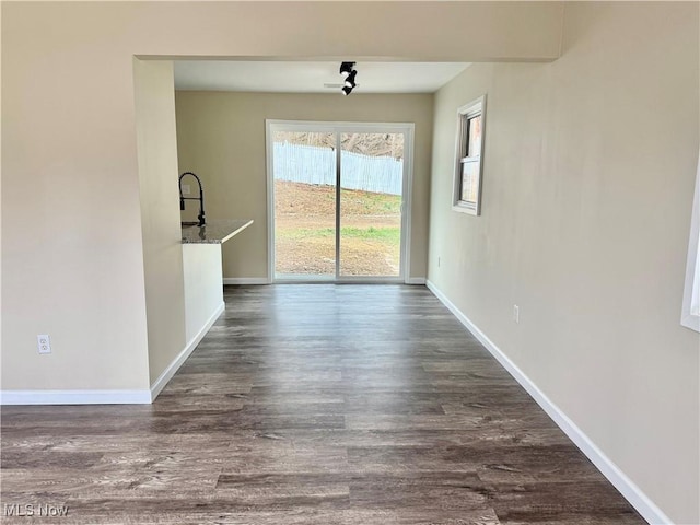 unfurnished dining area featuring baseboards, a sink, and dark wood-style flooring
