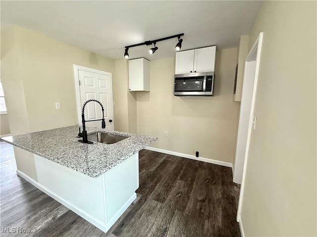 kitchen with dark wood finished floors, white cabinets, a sink, and stainless steel microwave