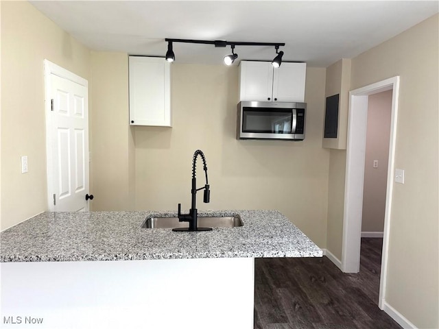 kitchen with dark wood-style flooring, stainless steel microwave, white cabinetry, a sink, and light stone counters