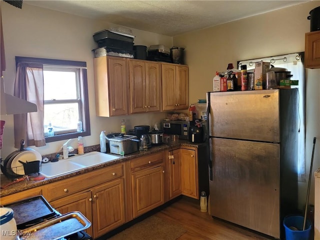 kitchen with a textured ceiling, wood finished floors, stainless steel appliances, dark countertops, and a sink