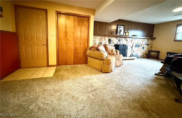 sitting room with a stone fireplace, carpet flooring, tile patterned flooring, and wooden walls