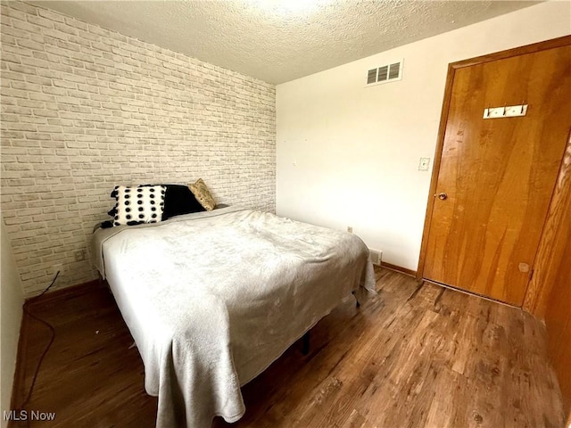 bedroom with brick wall, a textured ceiling, visible vents, wood finished floors, and baseboards