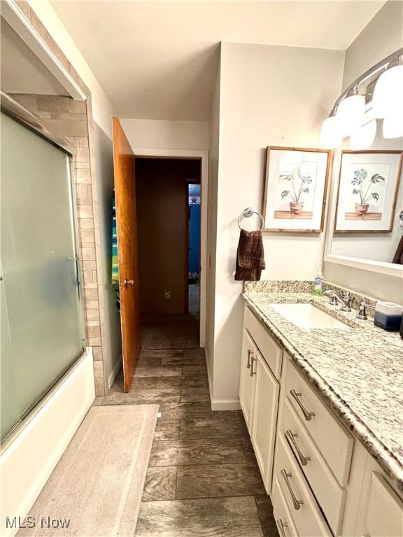 bathroom featuring bath / shower combo with glass door, baseboards, vanity, and wood finished floors