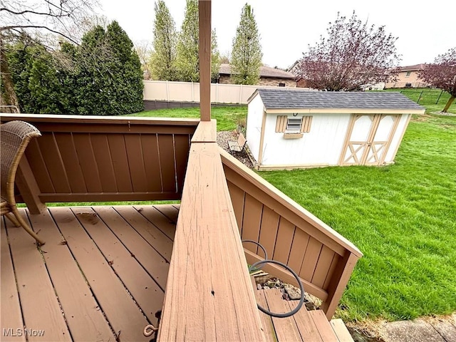 wooden terrace featuring an outdoor structure, a lawn, fence, and a shed