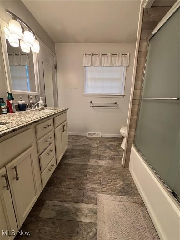 full bathroom featuring visible vents, wood finished floors, vanity, bath / shower combo with glass door, and toilet