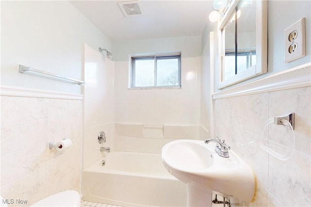 bathroom featuring tile walls, visible vents, washtub / shower combination, toilet, and a sink