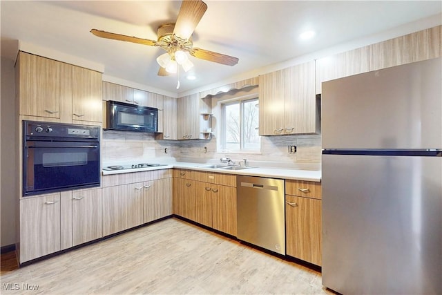 kitchen with decorative backsplash, light countertops, a sink, light wood-type flooring, and black appliances
