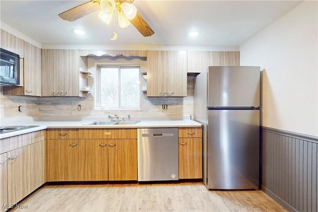 kitchen featuring light countertops, a sink, wainscoting, black appliances, and light wood-style floors
