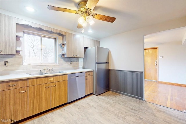 kitchen with a sink, wainscoting, light wood-style flooring, and appliances with stainless steel finishes