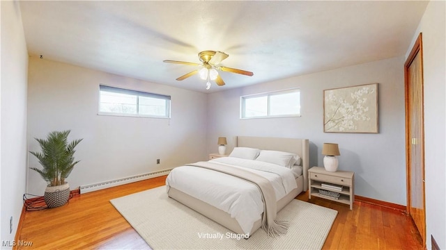 bedroom featuring baseboards, wood finished floors, a baseboard heating unit, and multiple windows