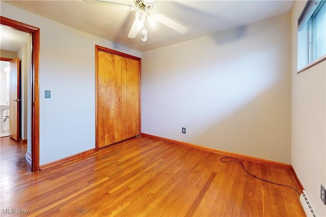 unfurnished bedroom with a closet, baseboards, ceiling fan, wood finished floors, and a baseboard heating unit
