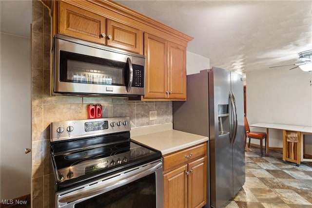 kitchen featuring stainless steel appliances, ceiling fan, brown cabinetry, baseboards, and light countertops