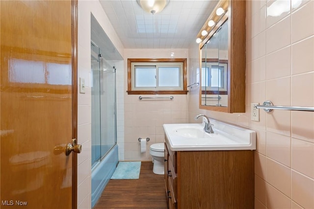 bathroom with tile walls, vanity, bath / shower combo with glass door, toilet, and wood finished floors