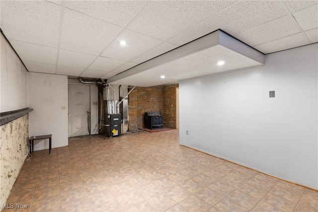 finished below grade area featuring a wood stove, a drop ceiling, heating unit, recessed lighting, and tile patterned floors