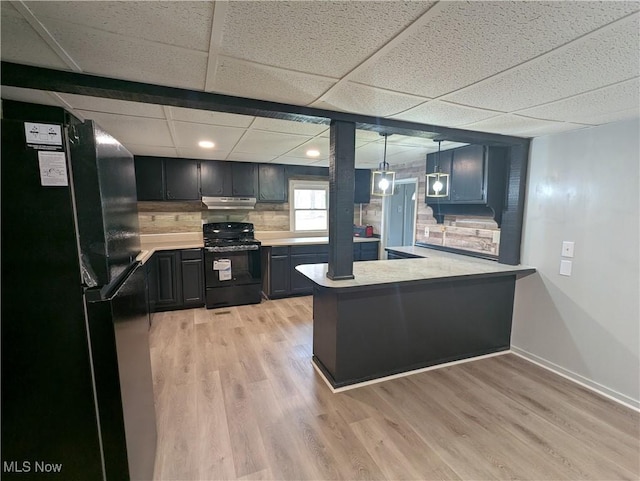 kitchen with light countertops, light wood-type flooring, under cabinet range hood, a peninsula, and black appliances