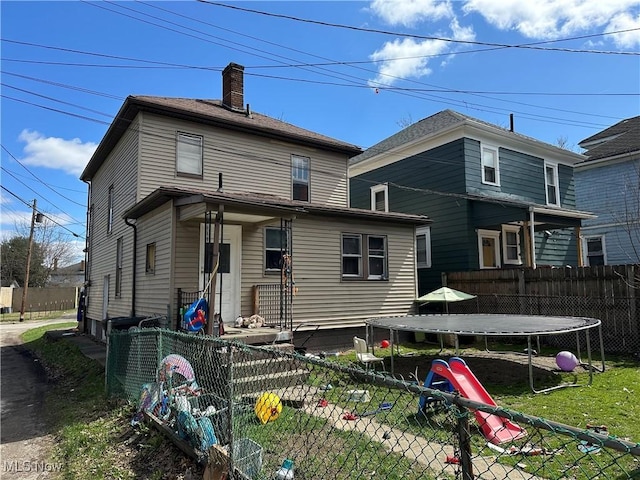 back of house with a chimney, fence, and a trampoline