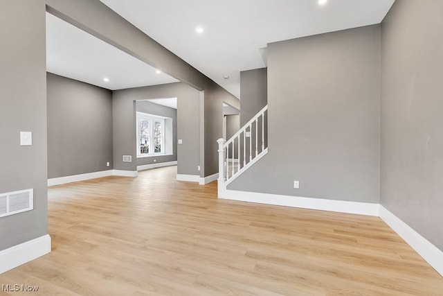 unfurnished room featuring baseboards, stairs, light wood-style flooring, and visible vents