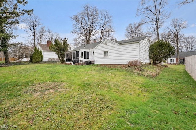 rear view of property with a lawn, a sunroom, and fence