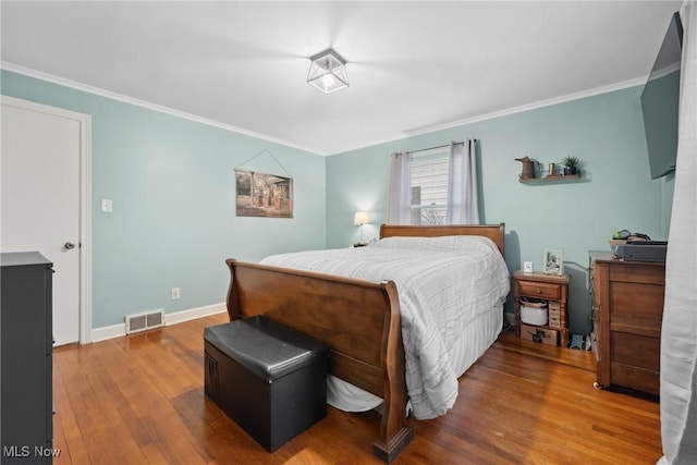 bedroom featuring wood finished floors, crown molding, baseboards, and visible vents