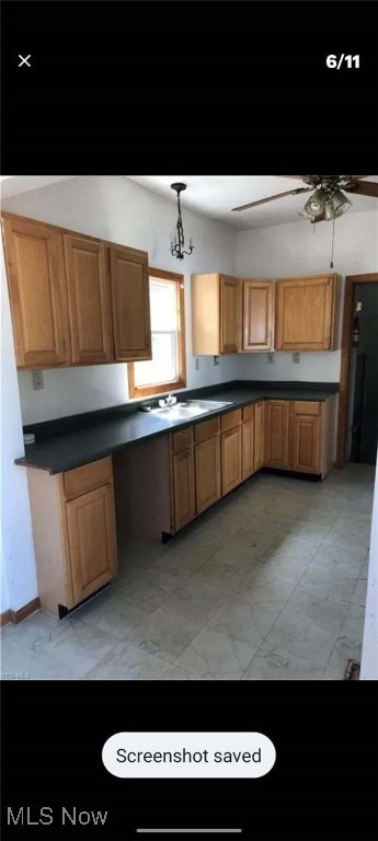 kitchen featuring ceiling fan with notable chandelier, dark countertops, a sink, and pendant lighting