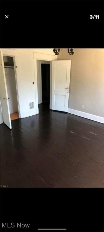unfurnished bedroom with dark wood-style flooring and visible vents