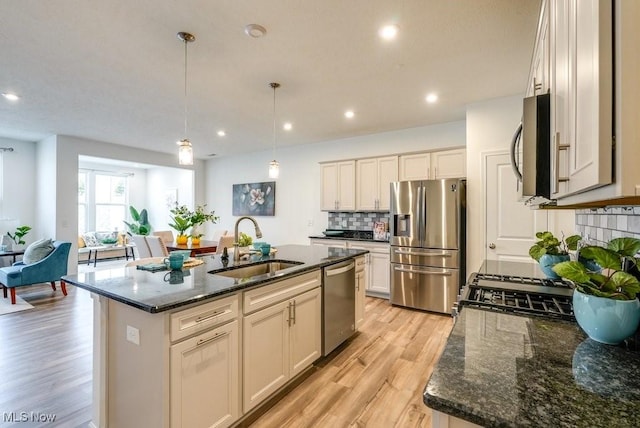 855-2 Dipper Ln, Aurora, OH 44202 - kitchen featuring appliances with stainless steel finishes, light wood-style flooring, dark stone counters, decorative backsplash, and a center island with sink