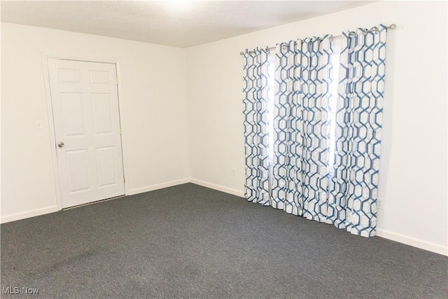 unfurnished room featuring baseboards and dark carpet