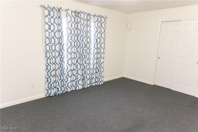 spare room featuring baseboards and dark carpet