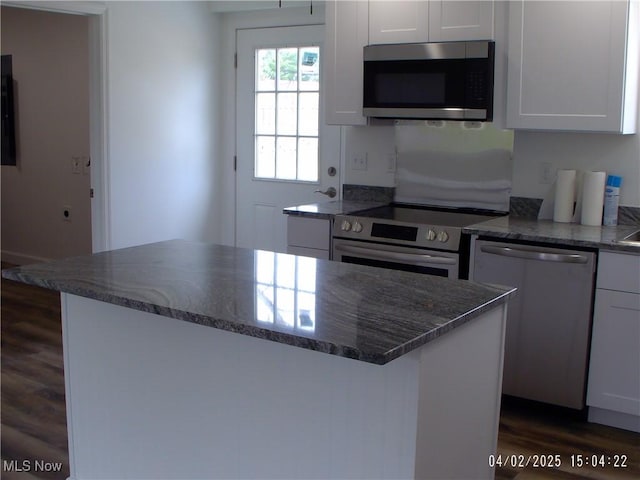 kitchen featuring white cabinets, stainless steel appliances, dark stone counters, a kitchen island, and dark wood finished floors