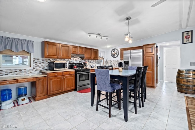 kitchen featuring under cabinet range hood, light countertops, stainless steel appliances, and tasteful backsplash