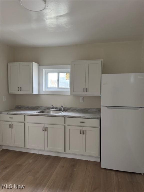 kitchen with light countertops, light wood finished floors, white cabinetry, a sink, and freestanding refrigerator